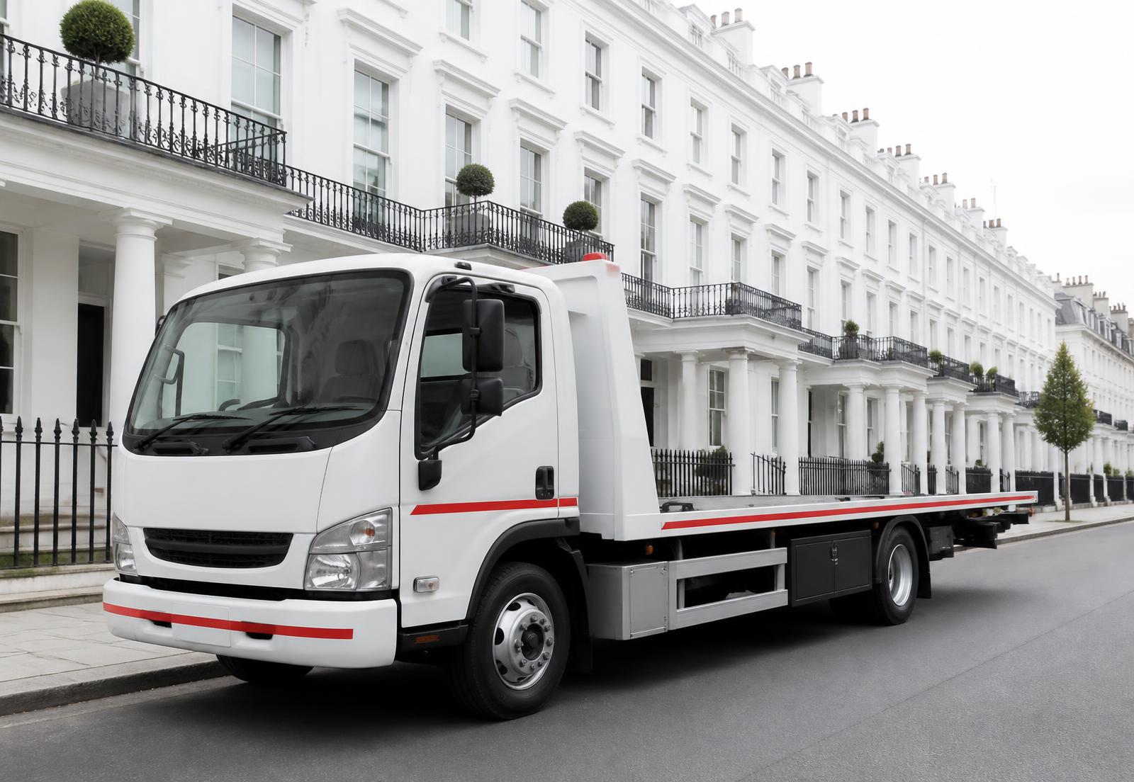 A white flatbed recovery truck parked on a London street in daylight