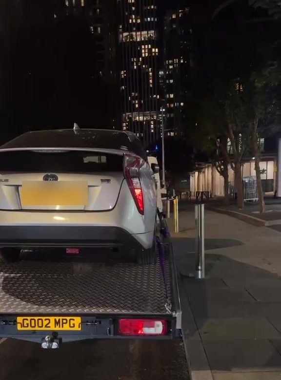A car on the MPG Recovery bed at night beside the towers at Canary Wharf